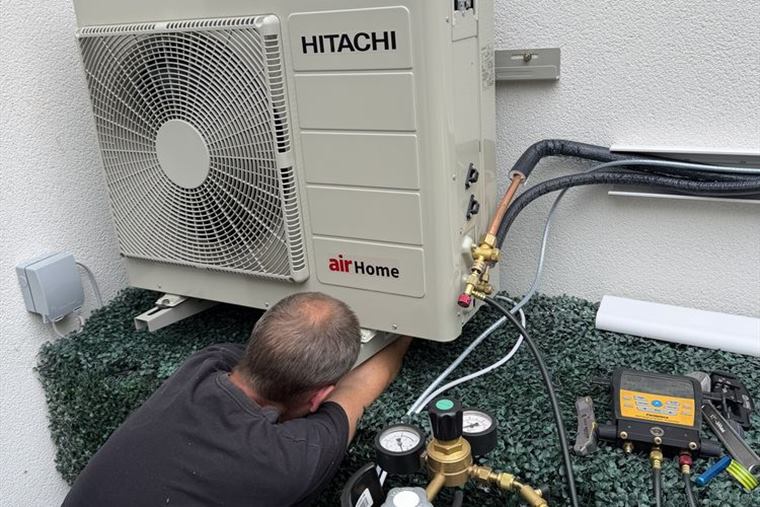 Engineer servicing a Hitachi airHome outdoor unit with test gauges